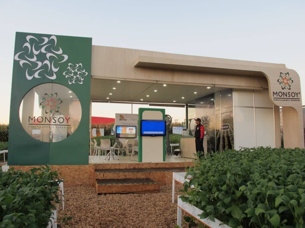 Estande externo da Monsoy montado pela LXBR, com portal verde, plataforma elevada e vitrine de cultivo de soja