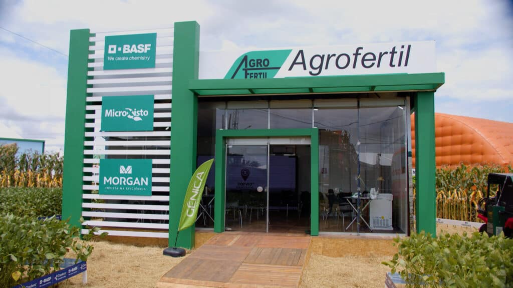 Estande envidraçado da Agrofertil montado pela LXBR no Show Safra, com pórtico verde, torre de sinalização e parcelas demonstrativas de milho e soja.