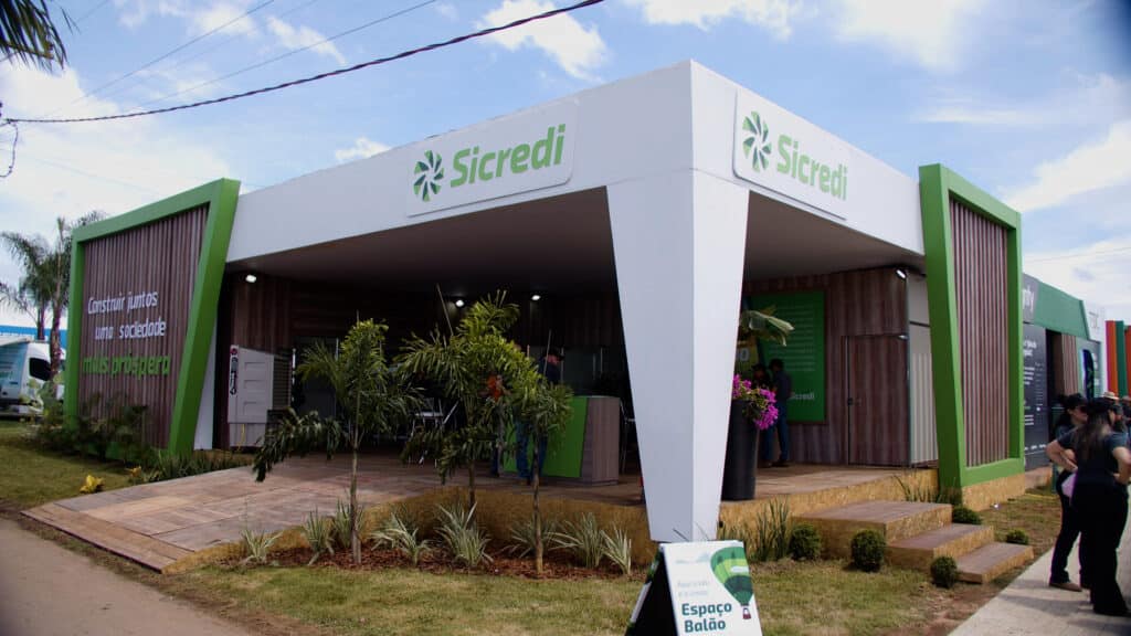 Estande da Sicredi no Show Safra, pavilhão aberto de cobertura branca com pilares verdes e deck elevado, montado pela LXBR
