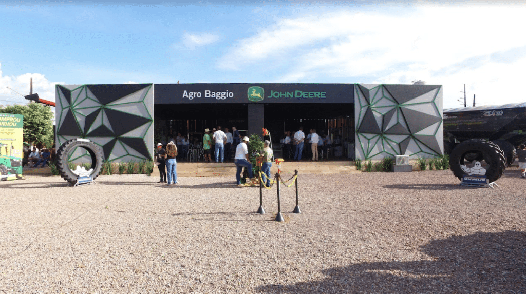 Estande da Agro Baggio (John Deere) montado pela LXBR no Norte Show, com fachada preta geométrica e pneus agrícolas na entrada.