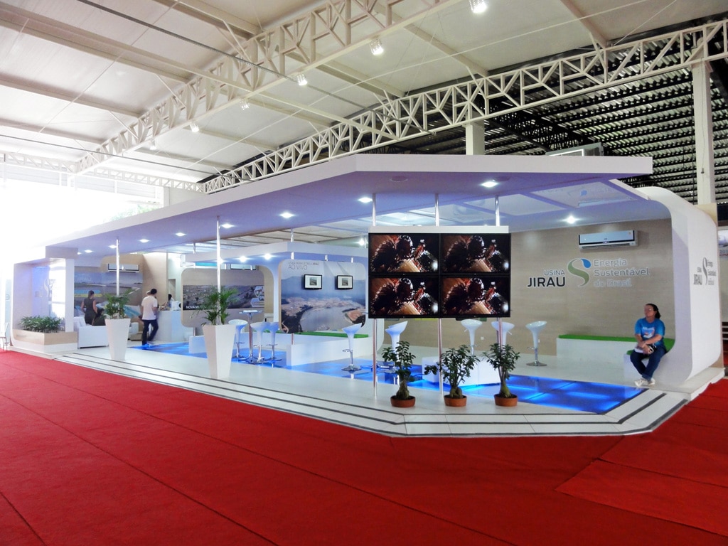 Estande em ilha da Energia Sustentável do Brasil montado pela LXBR, com cobertura suspensa branca, videowall e plataforma elevada