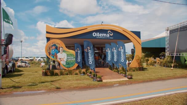 Estande da Oilema montado pela LXBR no Show Safra, com pórtico curvo escultural em azul-marinho e laranja e deck de madeira